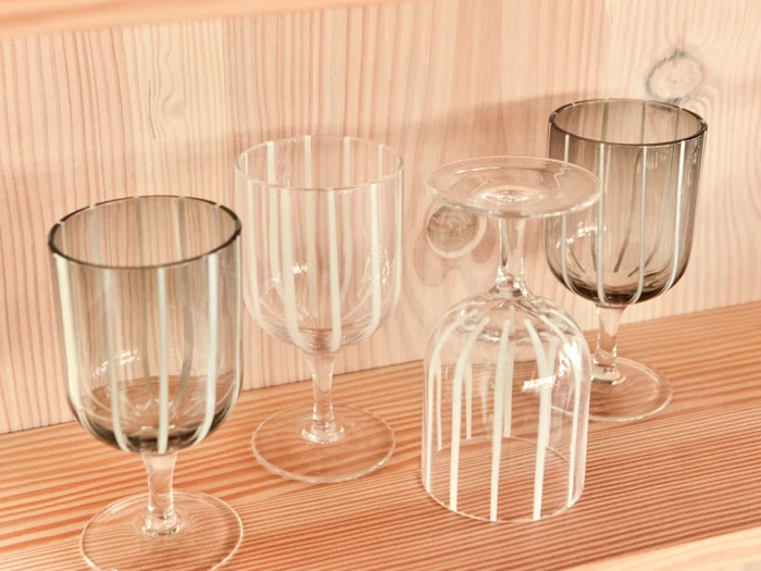 Fire gennemsigtige glas med lodrette striber står på en træhylde; det ene glas står på hovedet, mens de andre står oprejst.
