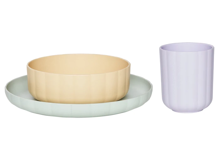 Et servise i pastelfarver bestående af en lysegrøn tallerken, en beige skål og en lyselilla kop, alle med en diskret ribbet struktur, på en hvid baggrund.