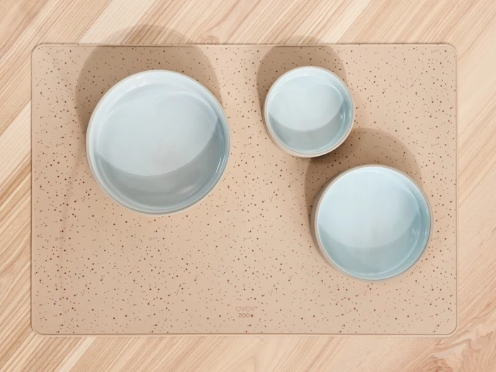 Tre lyseblå skåle i forskellige størrelser står på en beige, plettet rektangulær underlag på en lys træoverflade.