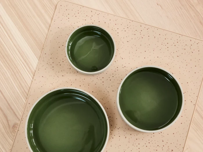Tre grønne skåle i forskellige størrelser er anbragt på en beige, plettet måtte, der ligger på en lys træoverflade, set ovenfra.