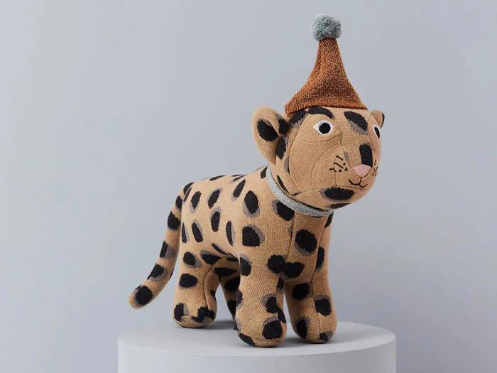 En plysleopard med sorte pletter og en festhat står på en hvid overflade mod en lysegrå baggrund.