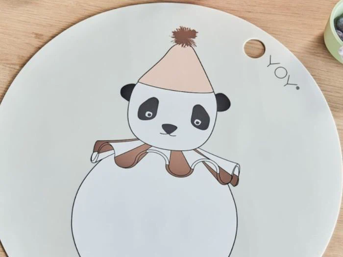 En rund dækkeserviet med en illustration af en panda med brun festhat og flæsekrave og ordet YOY. trykt ved siden af.
