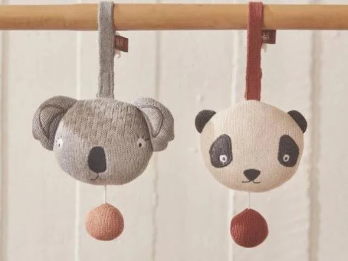 To strikkede dyrefigurer, en koala og en panda, hænger i stofløkker fra en træstang. Begge har runde hoveder og trækbånd med røde kugler fastgjort i bunden.
