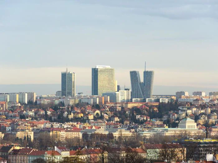 Et bybillede med en blanding af historiske lavhuse i forgrunden og moderne højhuse i baggrunden under en overvejende skyet himmel.