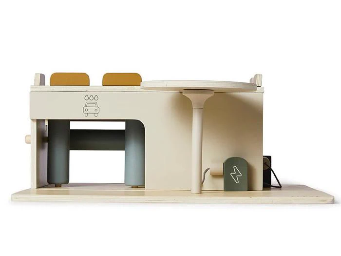 Minimalistisk legetøjsbilvaskestation i træ med et rundt bord, to solbrune sæder og illustrerede ikoner af en bil og en elektrisk ladestation.