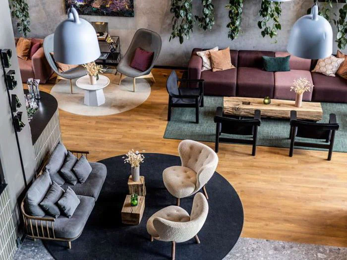 Moderne loungeområde med stilfulde sofaer, lænestole, runde tæpper, pendler, trægulv og grønne planter, der hænger på en betonvæg. Sofabordene er dekoreret med vaser med tørrede blomster.