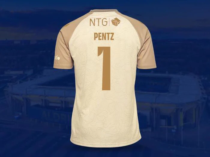 En beige og brun fodboldtrøje med navnet PENTZ og tallet 1 på ryggen, vist mod en sløret stadionbaggrund.