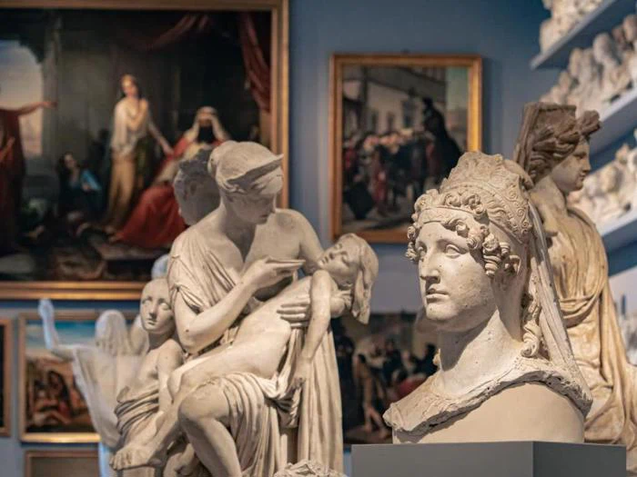Klassiske skulpturer og buster udstillet i et museumsgalleri med indrammede malerier på væggene i baggrunden.
