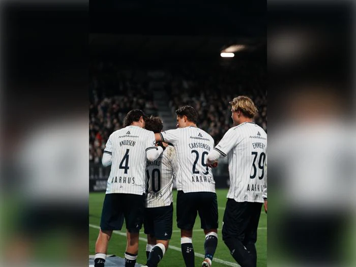 Fire fodboldspillere i hvidstribede trøjer, der fejrer et mål på banen.