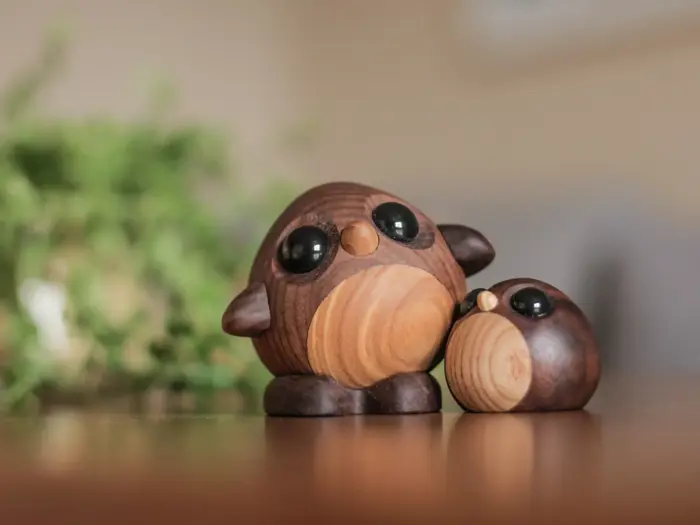 To uglefigurer af træ med store sorte øjne sidder på en glat overflade med en grøn, sløret baggrund.