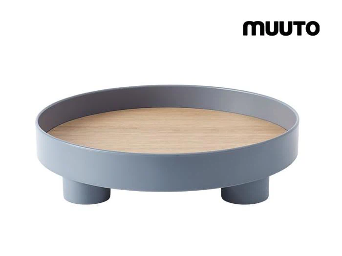 En rund, moderne bakke med en lys træbase, grå hævet kant og tre korte ben. Ordet MUUTO står med sort tekst i øverste højre hjørne.