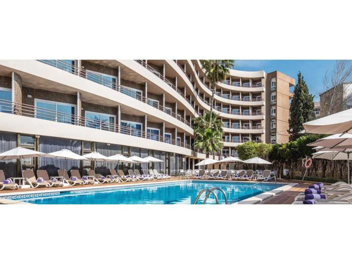 Et moderne hotel med buede balkoner med udsigt til en udendørs swimmingpool omgivet af liggestole og parasoller på en solrig dag.