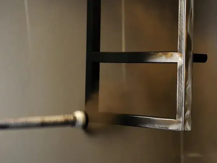 En metalramme bliver sprøjtemalet sort med en sprøjtedyse, der påfører maling på overfladen i et værksted eller et industrielt miljø.