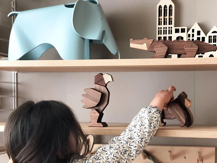 Et barn rækker ud efter dyrefigurer i træ på en hylde, mens en blå elefant og byggemodeller står på de øverste hylder.