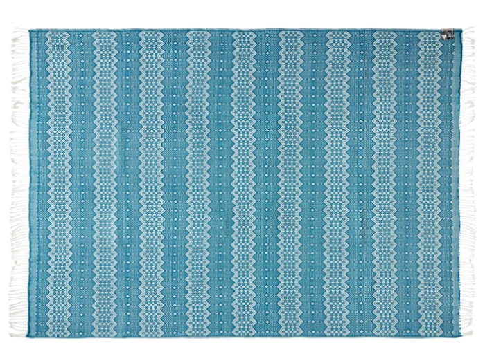Et rektangulært blåt vævet tæppe med hvide geometriske og zigzagmønstre, afsluttet med hvide frynser på de korte kanter.