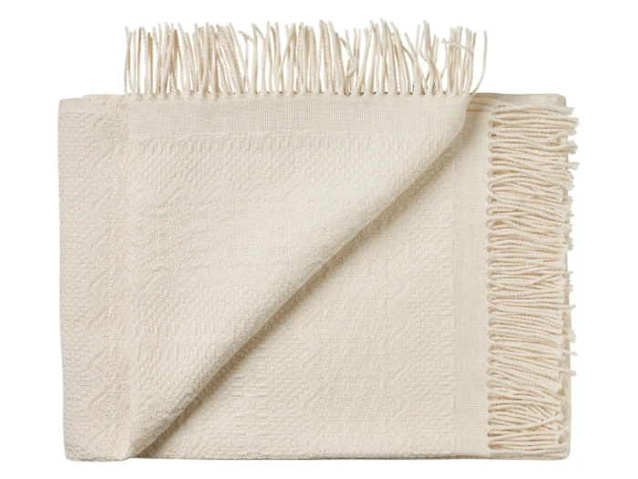 Et foldet cremefarvet vævet tæppe med frynsede kanter, vist mod en hvid baggrund. Det ene hjørne er vendt om, så man kan se strukturen på begge sider.