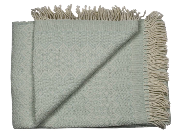 Et foldet lysegrønt vævet tæppe med et diskret geometrisk mønster og cremefarvede frynser langs den ene kant.