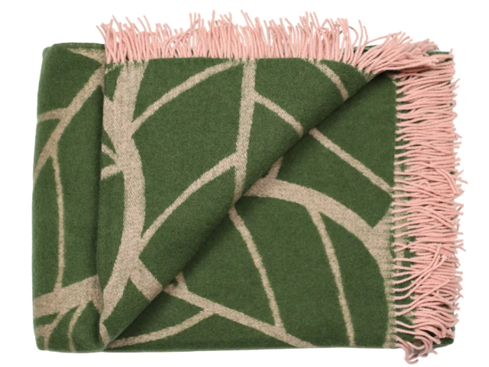 Et foldet grønt tæppe med lyserøde geometriske linjer og lyserøde frynser langs den ene kant.