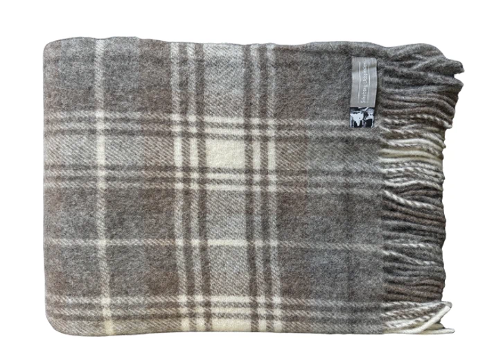 Et foldet, ternet uldtæppe i brune, beige og cremefarvede nuancer med frynsede kanter og en påsat etiket.