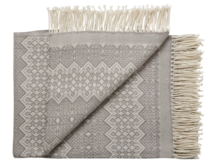 Et foldet gråt og hvidt mønstret vævet tæppe med frynsede kanter, delvist udfoldet for at vise det dekorative geometriske design.