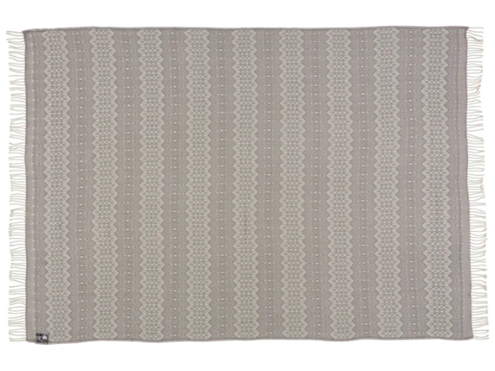 Et rektangulært vævet tæppe med et geometrisk mønster i beige og creme, frynsede kanter og et lille stofmærke i det ene hjørne.