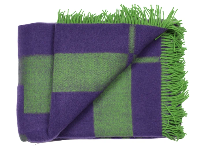 Et foldet tæppe med et stort grønt og lilla ternet mønster og grønne frynsede kanter.