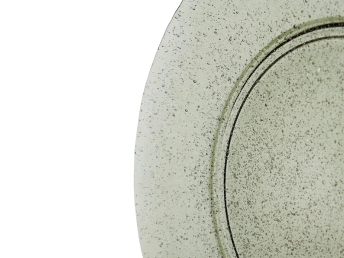 Et nærbillede af en struktureret, plettet rund plade med en metallisk eller keramisk finish, der kun viser en del af overfladen mod en hvid baggrund.