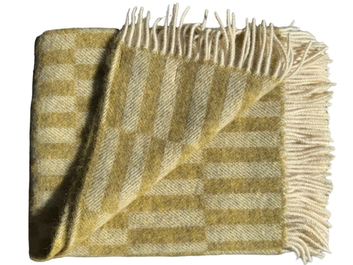 Et foldet, gult og cremefarvet ternet uldtæppe med frynsede kanter, vist på en hvid baggrund.