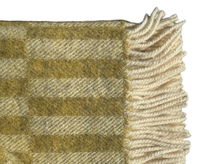 Et nærbillede af et uldtæppe med gult og beige ternet mønster og cremefarvede frynsekanter.