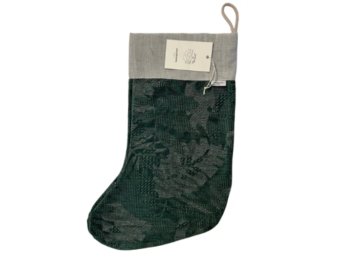 En grøn og grå mønstret julestrømpe med en beige manchet og en løkke til ophængning, vises fladt med et mærke fastgjort til manchetten.