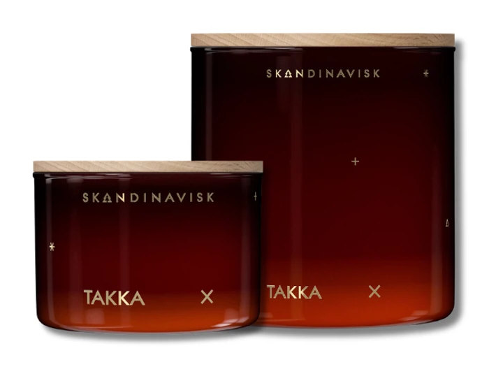 To ravfarvede glaskrukker med trælåg, mærket "SKANDINAVISK TAKKA", med minimale guldaccenter og et gradientdesign.