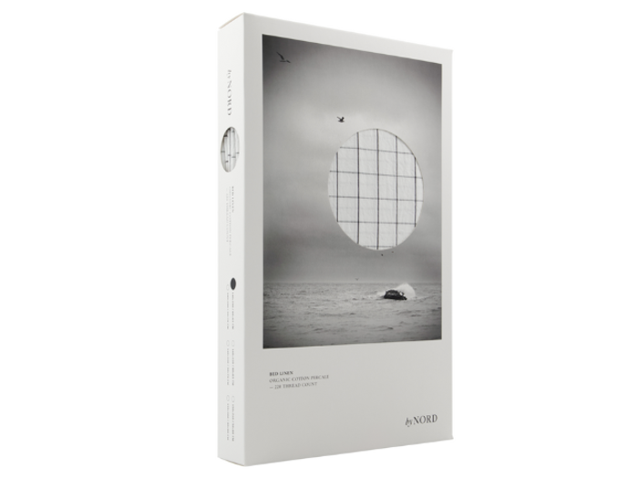 Minimalistisk emballage viser et havlandskab i gråtoner med fugle, en hval og et cirkulært gitteroverlay; teksten i bunden lyder by NORD.
