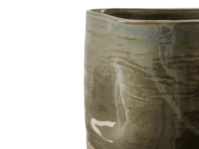 Nærbillede af en keramisk kop med en blank, marmoreret beige og lyseblå glasur mod en hvid baggrund.