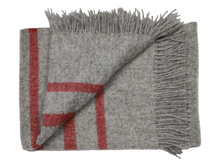 Et foldet gråt uldtæppe med røde striber og frynsede kanter, sirligt arrangeret på en hvid baggrund.