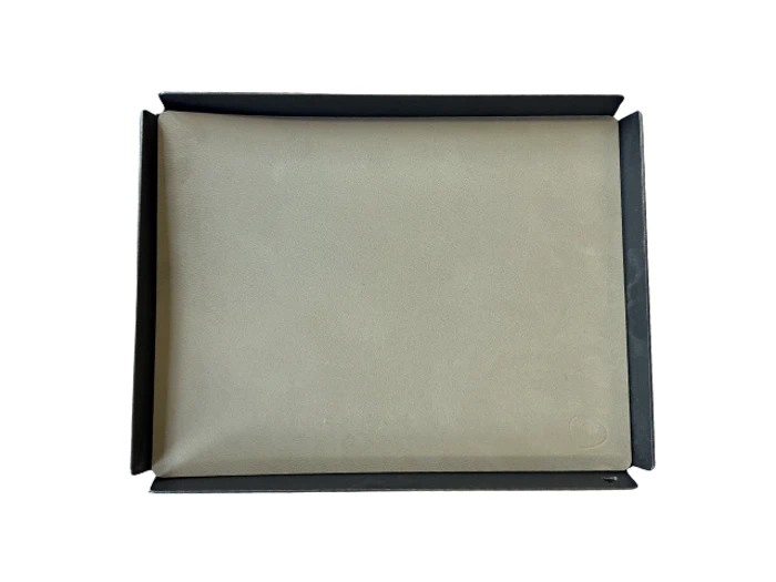 Et lukket beige laptop-sleeve ligger inde i en åben sort kasse på en hvid baggrund.
