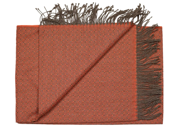 Et foldet brændt orange vævet tørklæde med små prikker, brune frynsede kanter og et hjørne, der er vendt om for at vise bagsiden.