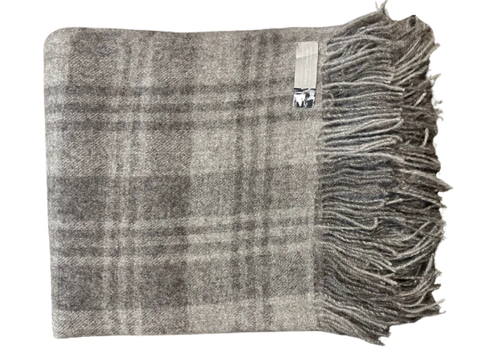 Et foldet gråternet uldtæppe med frynser på den ene side og en lille etiket i nærheden af frynserne.