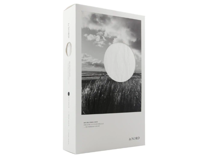 En hvid æske med et sort-hvidt foto af en mark og en himmel, som indeholder et sengesæt af mærket byNORD. Emballagen er minimalistisk og elegant.