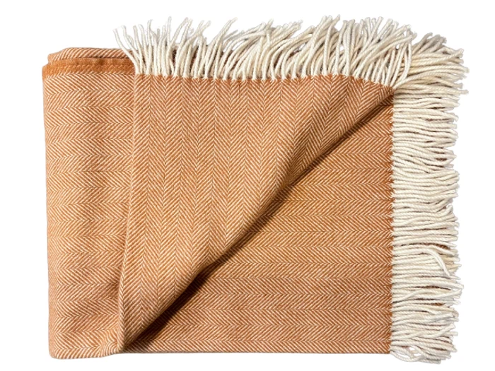 Et foldet orange sildebensmønstret tæppe med hvide frynser langs den ene kant.