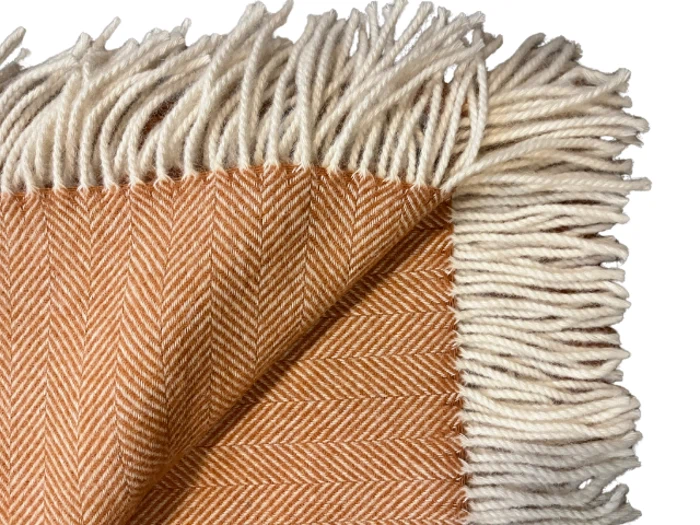 Nærbillede af et vævet orange og cremefarvet sildebensmønstret tæppe med cremefarvede frynser på kanterne.