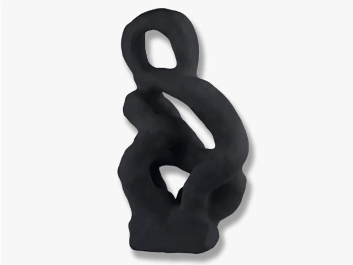 Abstrakt sort skulptur med glatte, buede former og en løkke i toppen, som står på en almindelig hvid baggrund.