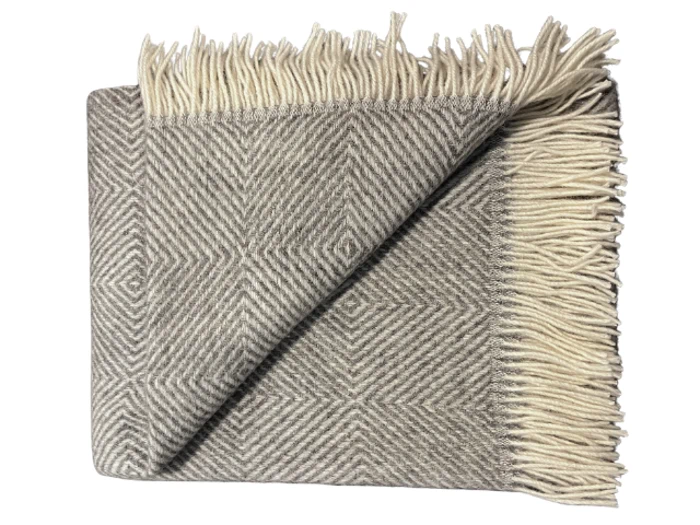 Et foldet gråt og hvidt sildebensmønstret tæppe med cremefarvede frynser på kanterne, vist på en hvid baggrund.