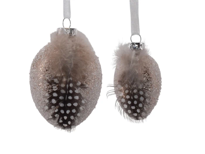 To glitrende, ovale julekugler med påsatte brune og hvide plettede fjer, der hænger i hvide bånd.