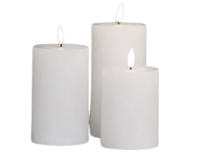 Tre hvide bloklys i forskellige højder er tændt og sat sammen mod en almindelig hvid baggrund.