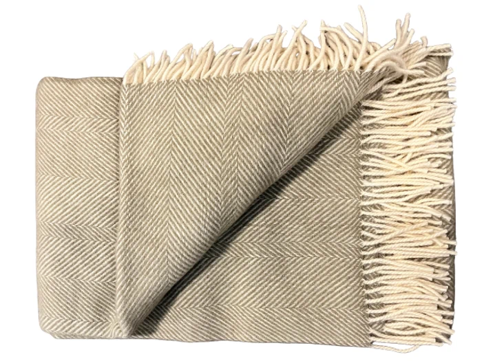 Et foldet beige sildebensmønstret tæppe med cremefarvede frynser på den ene kant.