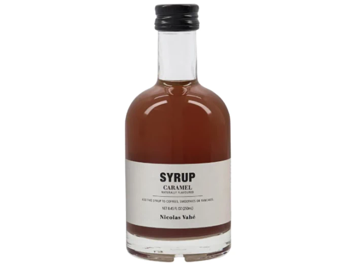 En klar glasflaske med karamelsirup med sort hætte og en hvid etiket, hvor der står Syrup Caramel by Nicolas Vahé.