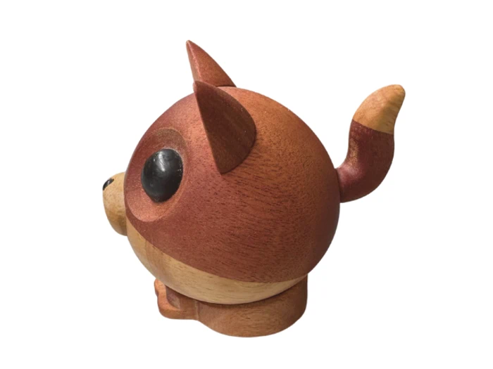 En rund dyrefigur af træ med store sorte øjne, spidse ører og en stribet hale, der ligner en tegneserie-vaskebjørn eller -ræv, på en hvid baggrund.