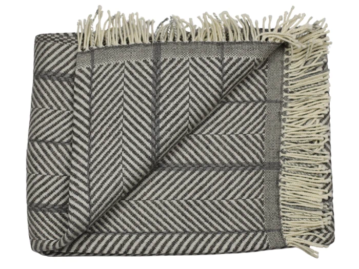 Et foldet, frynset tæppe med et gråt og hvidt sildebensmønster. Det ene hjørne er vendt om, så stoffets bagside kommer til syne.
