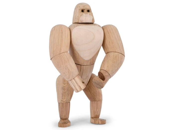 En gorillafigur af træ med bevægelige led står oprejst mod en almindelig hvid baggrund.