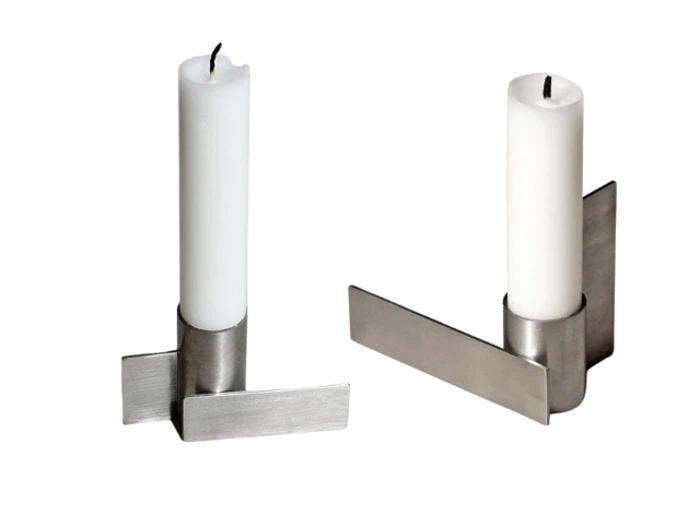 To hvide stearinlys i moderne, minimalistiske sølvmetalholdere med flade, kantede baser på en hvid baggrund.